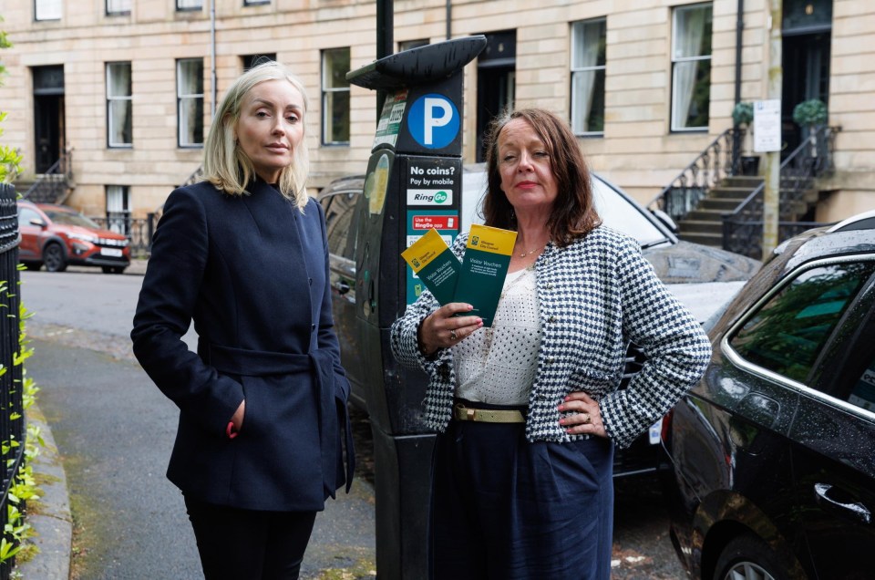 Two women stand by a parking meter, holding visitor parking vouchers.