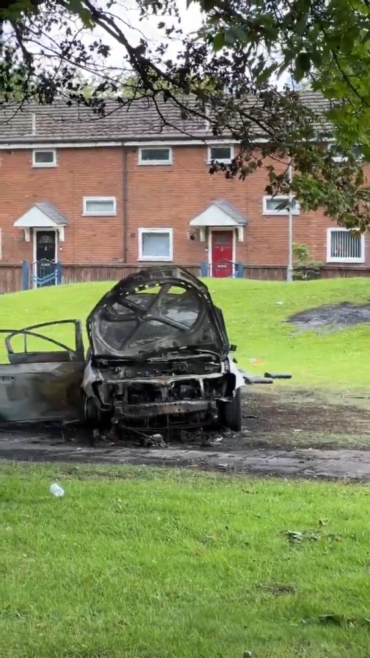 Burned-out car in front of residential buildings.