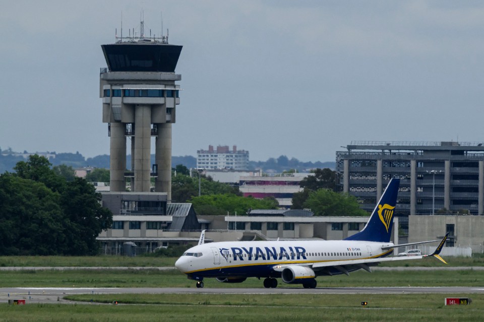 Ryanair plane taxiing on an airport runway near the control tower.