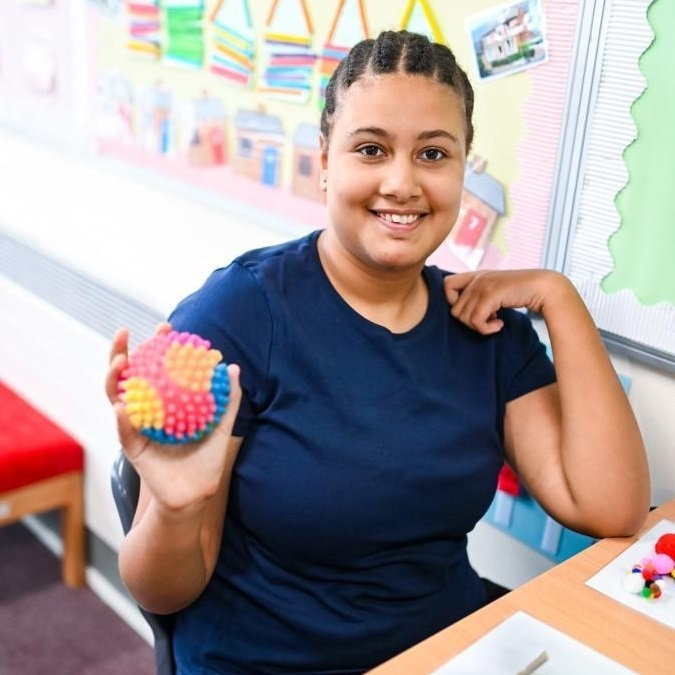 A young woman holds a multicolored textured ball.