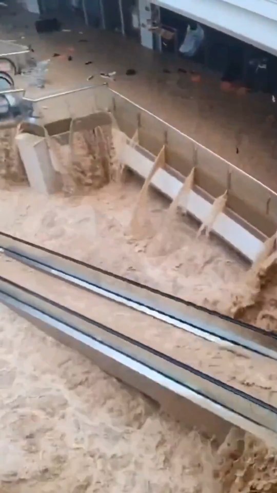 Floodwaters rushing through a shopping mall, submerging escalators.