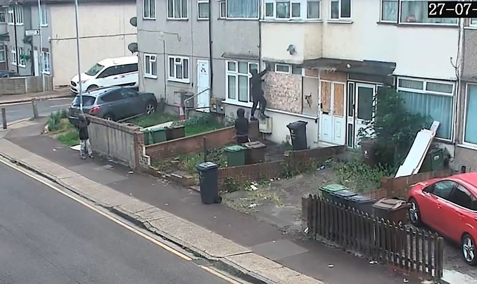 CCTV footage of a house with boarded-up windows, showing two people near the property.