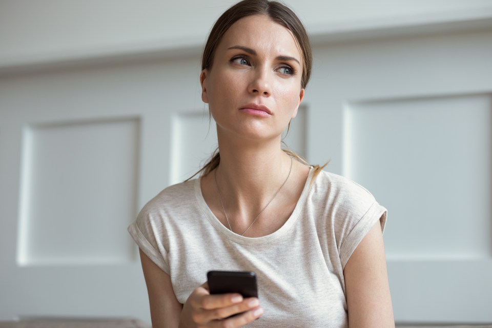 A pensive woman looking away while holding a smartphone.
