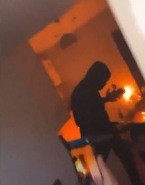 A person in a hooded sweatshirt stands in a room engulfed in orange light.