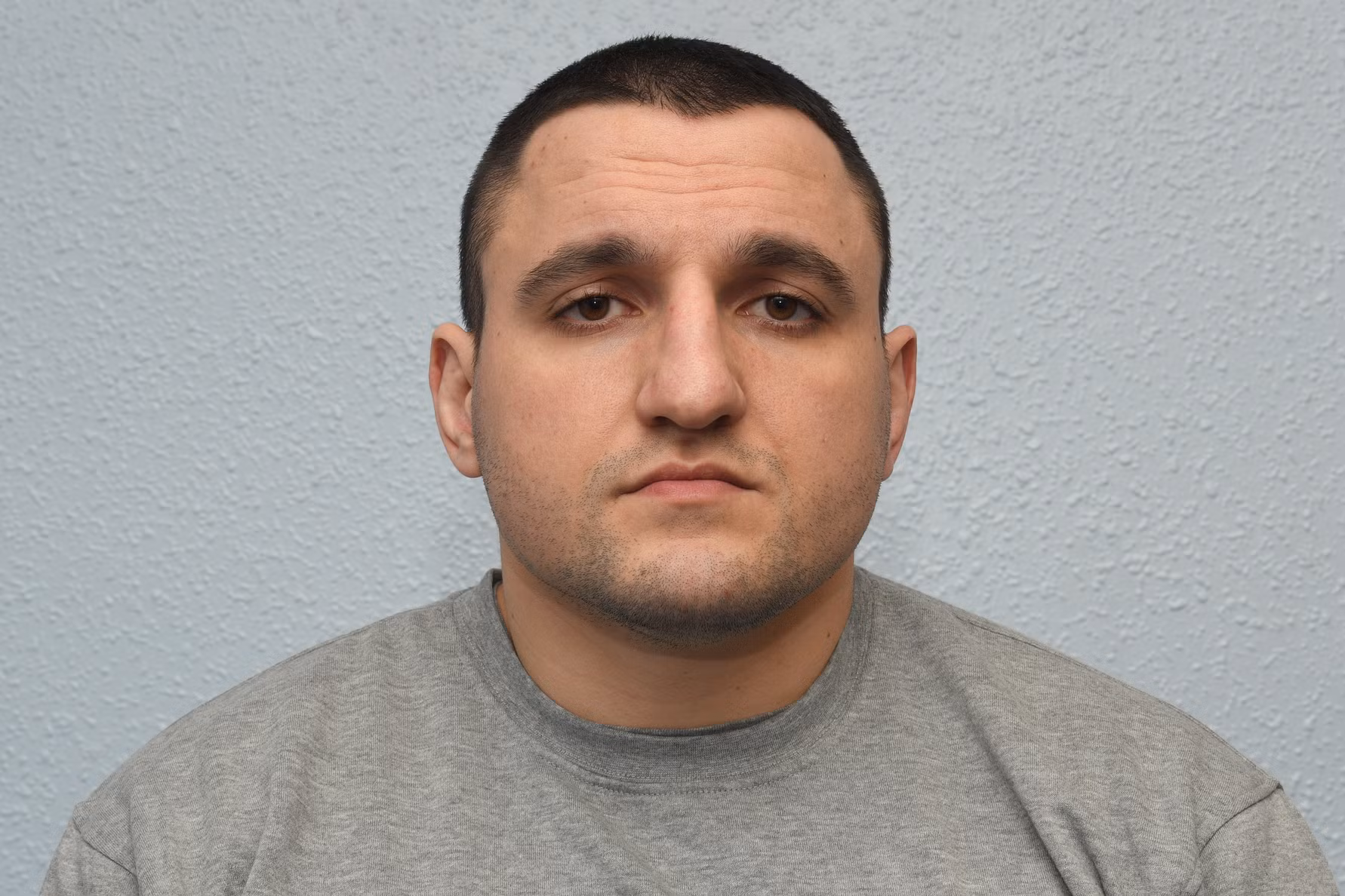 Mugshot of a man with short brown hair wearing a gray shirt.