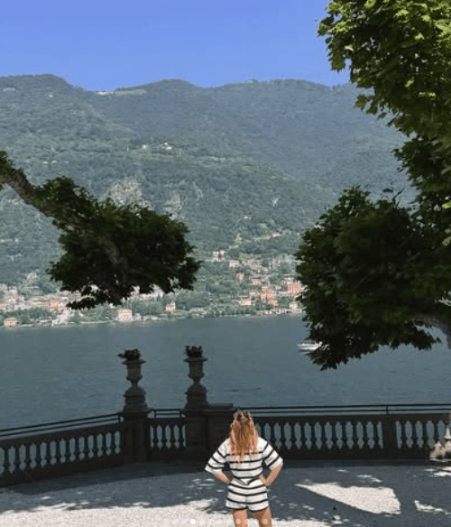 Woman overlooking lake and mountains from a stone terrace.