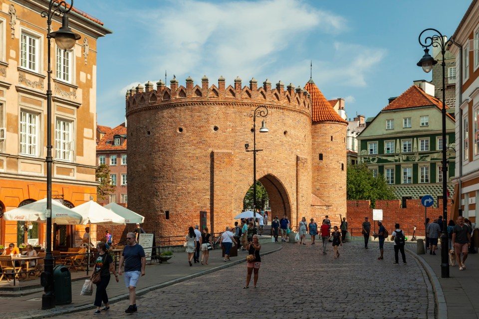 Brick gate in Warsaw's New Town with people walking by.