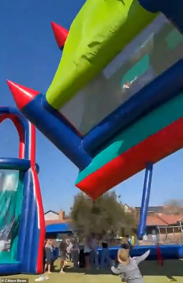 A shocked attendant helplessly watches as one of the children trapped on the inflatable is unable to hold on and plummets to the ground below