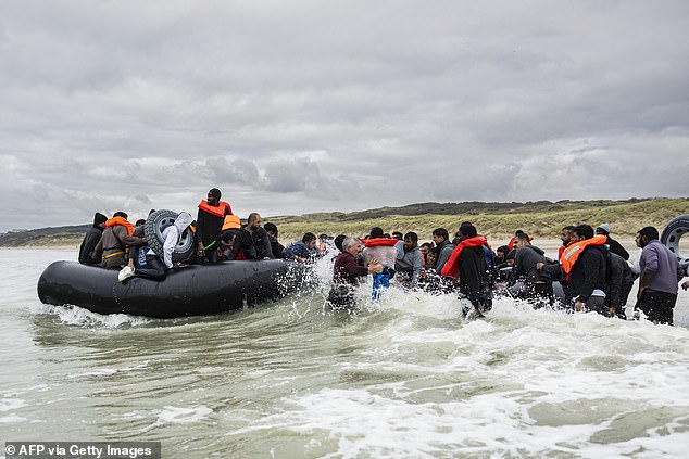 Migrants - one of them wearing a rubber ring - rush a dinghy in an attempt to cross the Channel last year