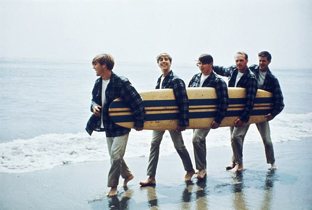 Brian Wilson, the genius of The Beach Boys whose soaring falsetto gave the world Good Vibrations, endured a life of horrific mental torment. Pictured: American Rock and roll band The Beach Boys walk along a beach holding a surfboard during a photoshoot for their debut album, 'Surfin' Safari', Los Angeles, California, August 1962. Left to right: Dennis Wilson, David Marks, Carl Wilson, Mike Love and Brian Wilson