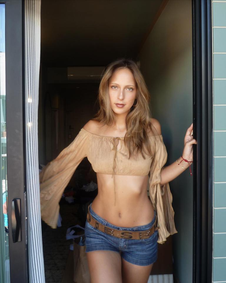 Woman in tan top and denim shorts standing in doorway.