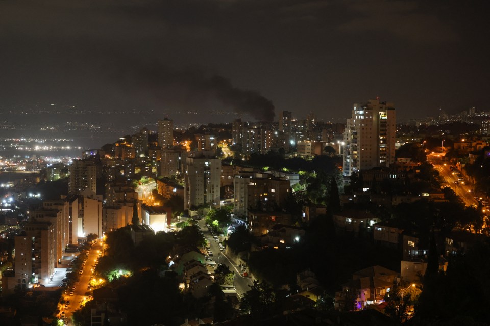 Nighttime view of Haifa, Israel, with smoke billowing from a missile attack.