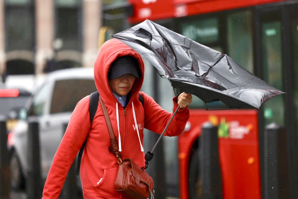 Person battling strong winds and rain while holding an umbrella in London.