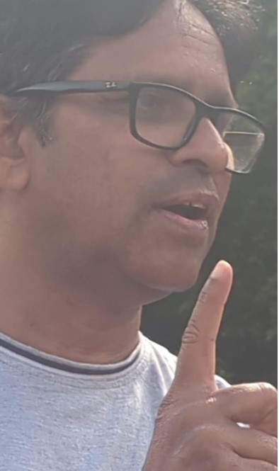 Man wearing glasses speaking with his index finger raised.