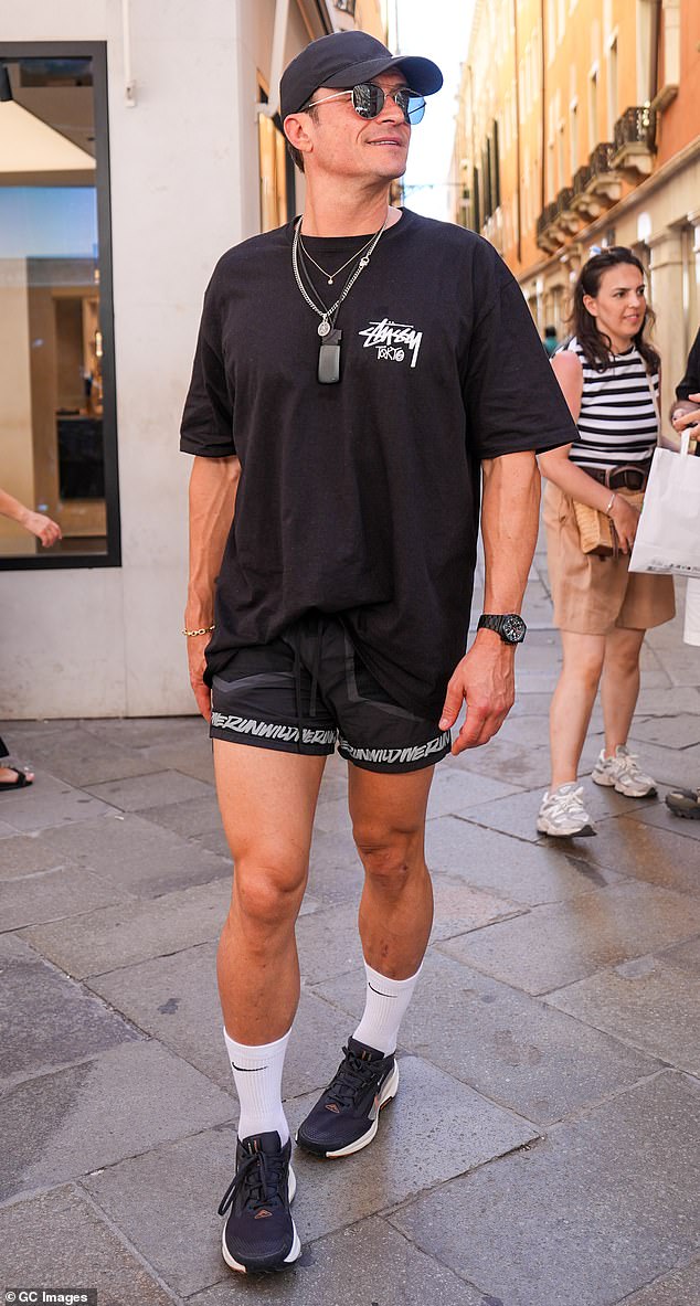 Whether's it is because he's still healing from his break-up from Katy Perry or just because he really did think this was a good look, Orlando Bloom, 48, decided to step out on his third day in Venice wearing very short Nike shorts. Paired with a Stüssy Tokyo shirt, baseball cap, sunglasses, and three different chains, Bloom looks more ready to play a sport than to attend whatever wedding festivity the Bezos family have planned