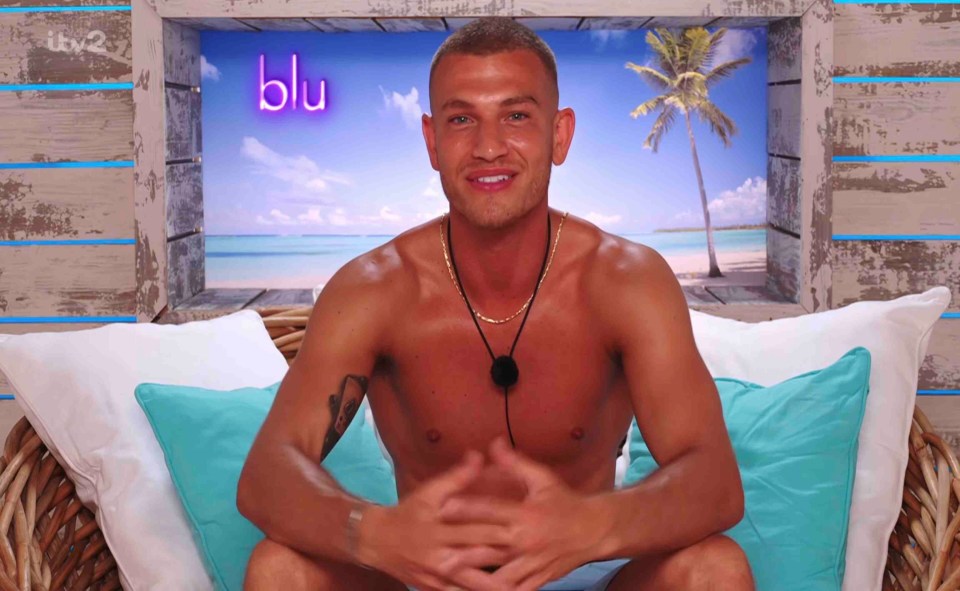 A man sits shirtless on a wicker couch, smiling at the camera.  A tropical beach scene is visible in the background.