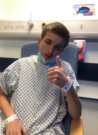 Teenage boy in hospital gown giving thumbs up.