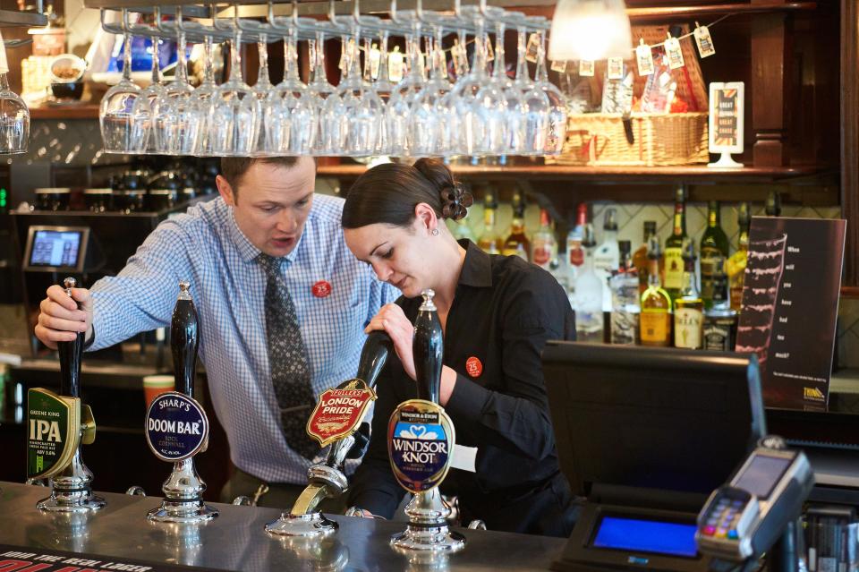 Two bartenders pulling pints of beer.