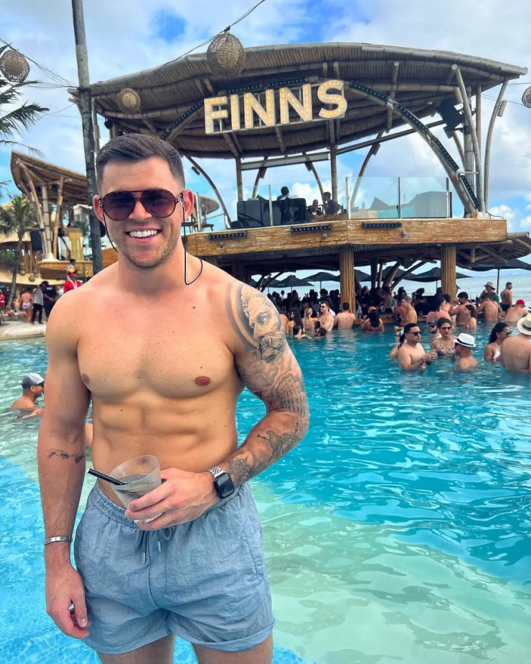 Man in swim trunks holding a drink by a pool at Finns Beach Club.
