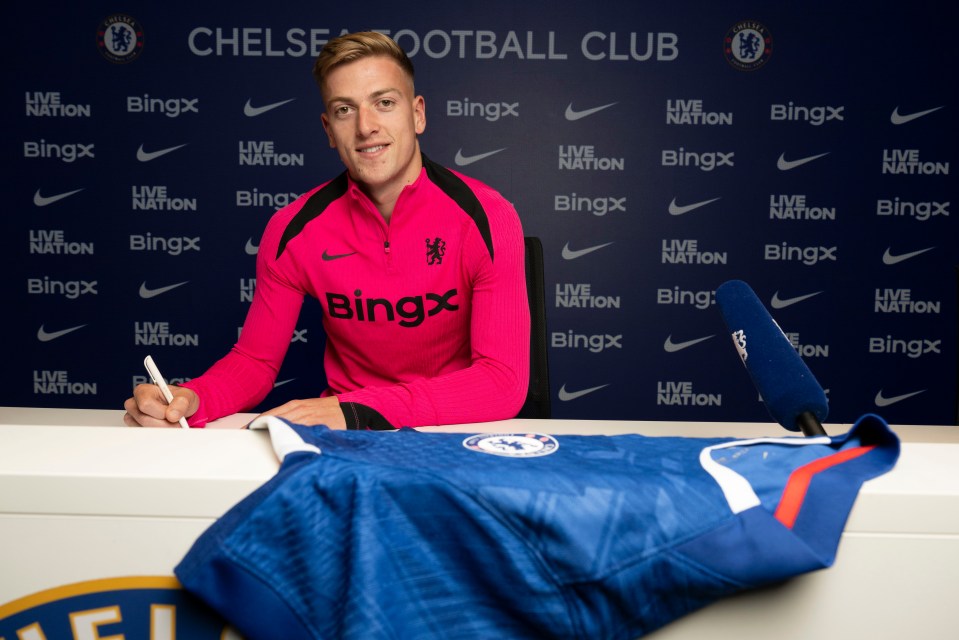 Liam Delap signing a Chelsea jersey at a press conference.