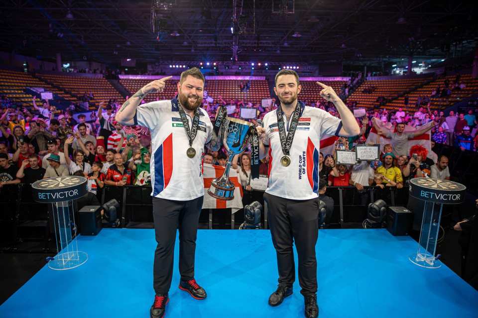 Michael Smith and Luke Humphries holding the World Cup of Darts trophy.