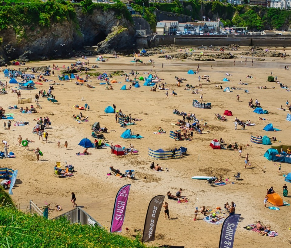Aerial view of a crowded beach with people sunbathing, swimming, and playing.