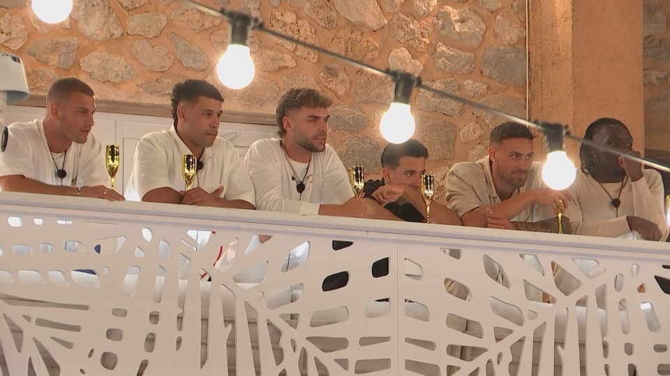 Six men from Love Island watching from behind a white railing.