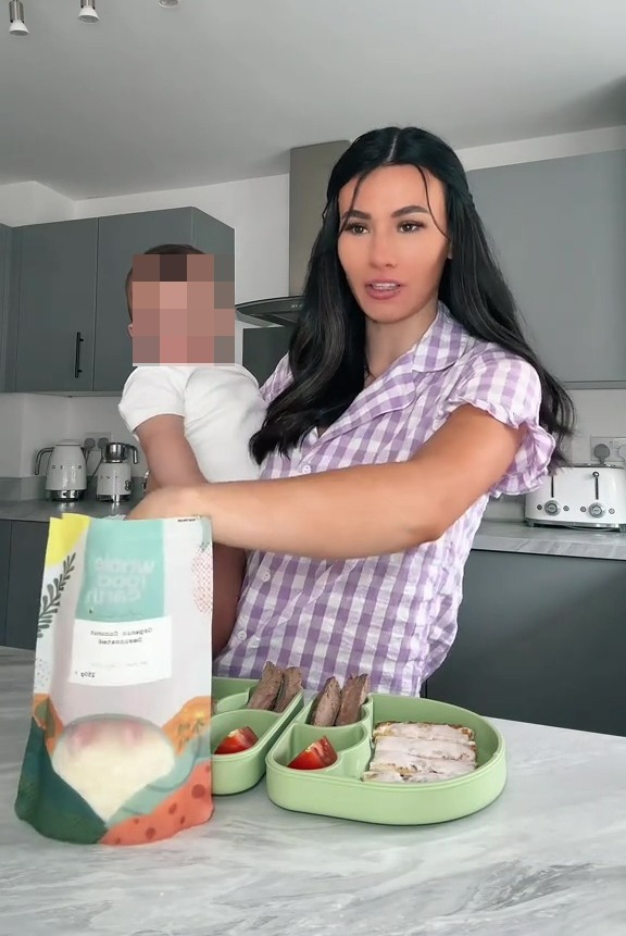 A woman holding a baby shows off her twins' breakfast, which includes meat and what appears to be mashed potatoes.