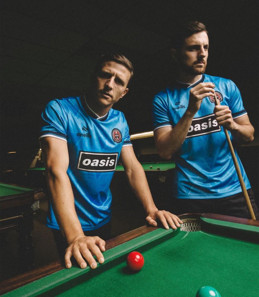 Two men in blue jerseys leaning on a pool table.