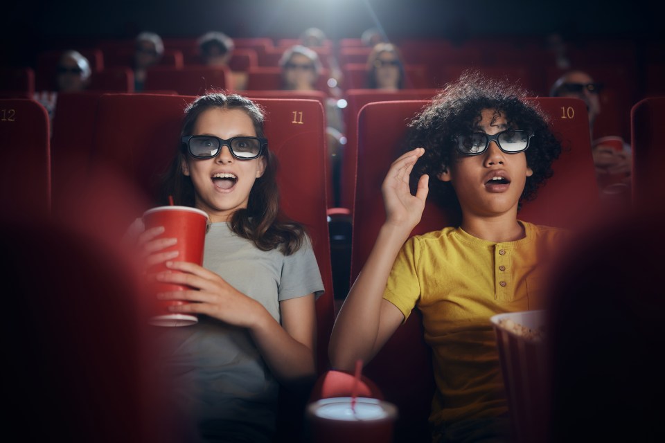 Two children wearing 3D glasses watch a movie in a cinema.