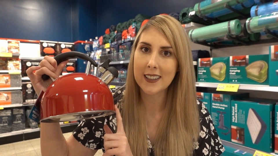 Woman holding a red whistling kettle in a store.
