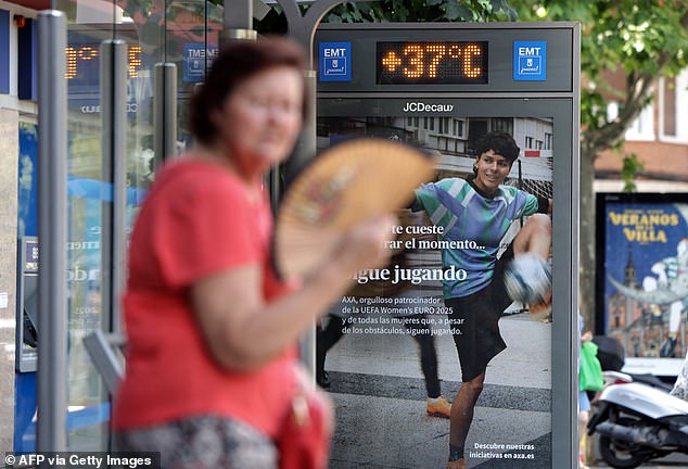 Pictured: A woman cools herself off using a fan at a bus stop showing a temperature of 37C during a heatwave in Madrid, on July 1, 2025