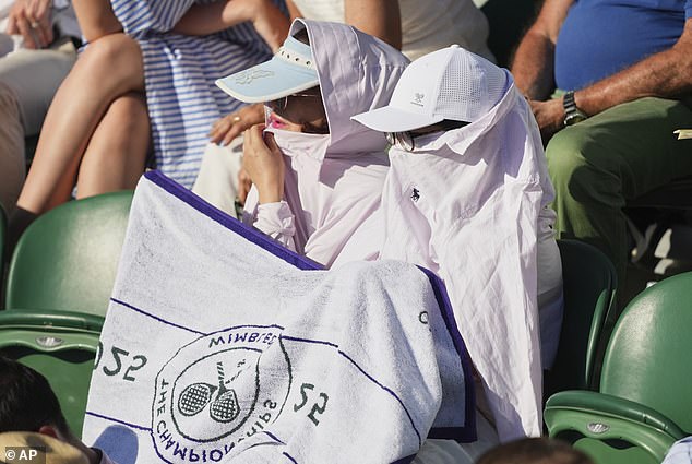 Spectators cover themselves from the sun on day one at the Wimbledon Tennis Championships in London, Monday, June 30, 2025. (AP Photo/Joanna Chan)