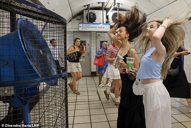 Two young women cool off in front of a large fan at a London Underground station yesterday morning