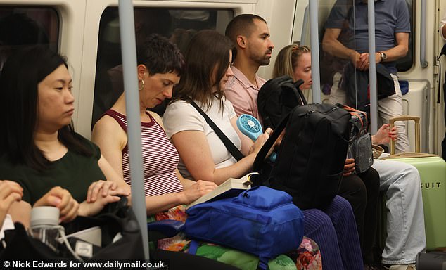 Hot weather on the Jubilee line in London yesterday morning as commuters use fans to cool down