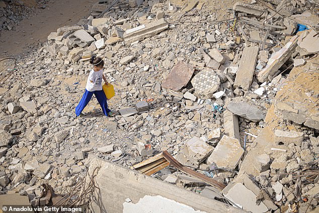Pictured: A 10-year-old girl living with her father in a destroyed building in the Nasr neighborhood west of Gaza City carries water