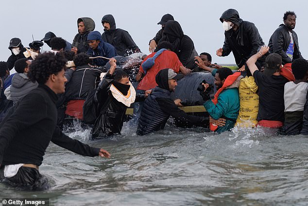One terrified migrant was seen cowering as the masked thug with a rubber ring around his neck brandished the long stick