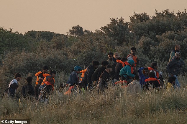 A large group of migrants emerge from the sand dunes before heading back in again as the police arrive