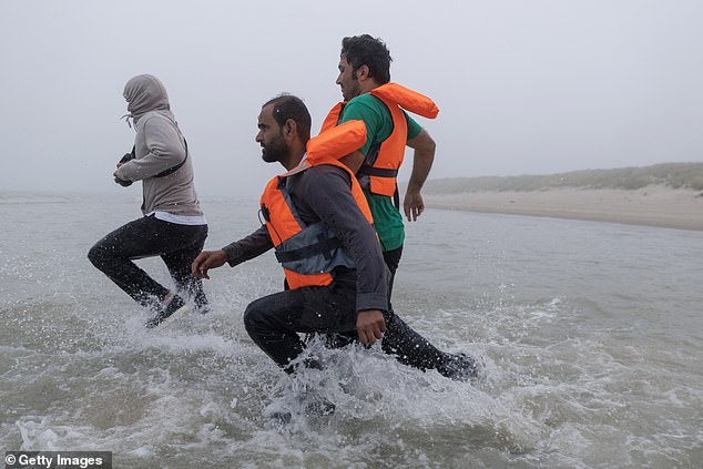 Migrants run into the water to be collected by a small boat in the fog early this morning