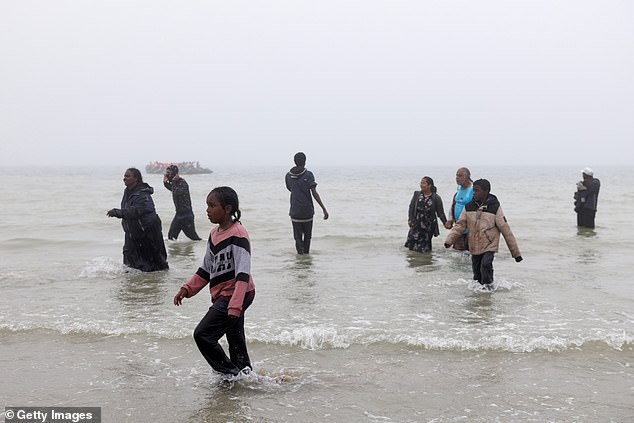 Families and children walk back to shore in the fog after failing to board a small boat
