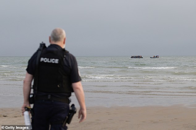 A police officer watches on as a Maritime Gendarmerie rib approaches a small boat full of migrants heading in to the English Channel