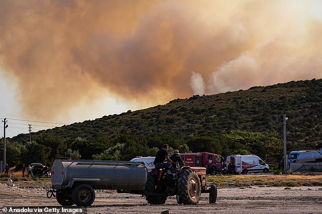 People living in the area support the teams by carrying water to the area with their tractors as smoke rises from burning trees while air and land intervention continues against the fire that broke out in the forest area in Cesme district of Izmir