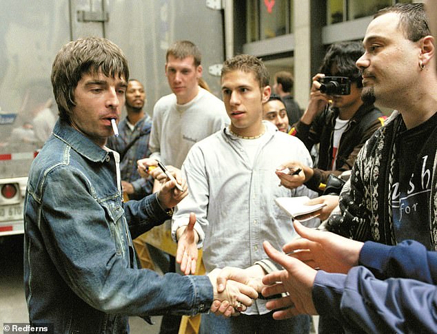 A vintage shot of Noel casually smoking a cigarette while signing autographs perfectly captures his effortlessly cool, rock-star aura