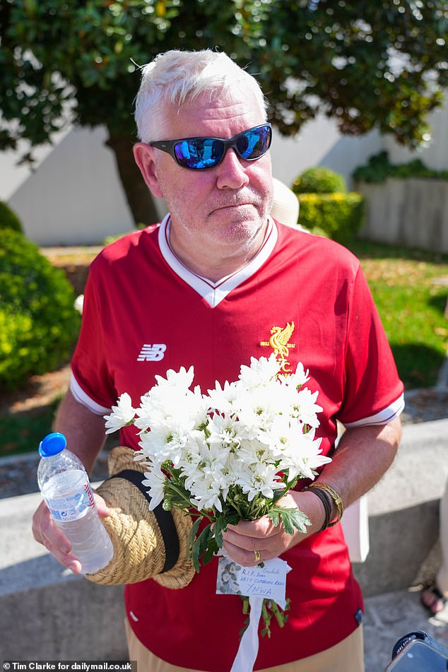 A Liverpool fan holds a floral tribute to Diogo Jota bearing the acronym YNWA - short for the club's motto 'You'll Never Walk Alone'