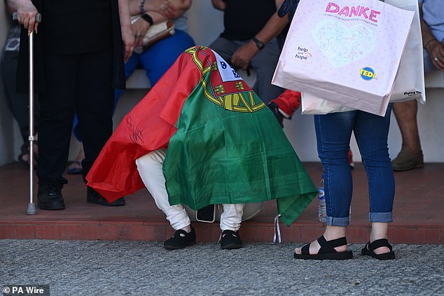 A devatstaed fan hides underneath a Portugal national flag as they deal with the shock of Jota's sudden death