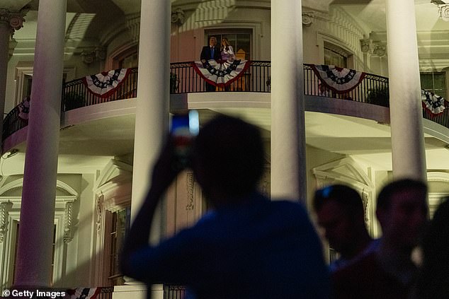 An attendee at the White House's Fourth of July celebration in the South Lawn takes a photo of President Donald Trump and first lady Melania Trump watching the fireworks from the Truman Balcony