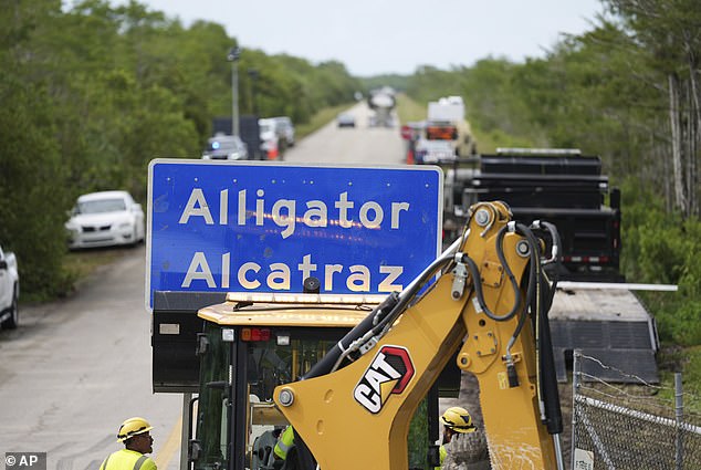 A loader holds a sign reading "Alligator Alcatraz" in its bucket as workers install it at the entrance to a new migrant detention facility in Florida