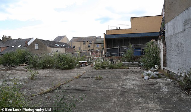 Outside the shopping centre, a stretch of brown belt land lies derelict and weeded