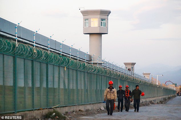 As many as one million ethnic Uighurs and other mostly Muslim minorities are believed to be held in a network of internment camps in Xinjiang. Pictured: Workers walk by the perimeter fence of what is officially known as a vocational skills education centre in in Dabancheng, Xinjiang