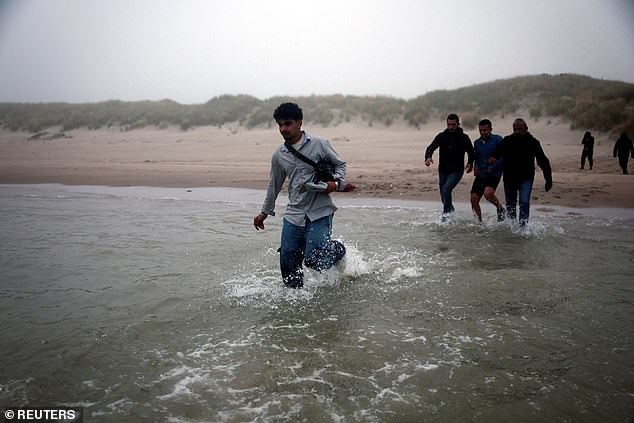 A group of migrants walk through the water to reach an inflatable dinghy in an attempt to cross the English Channel to reach Britain on July 2
